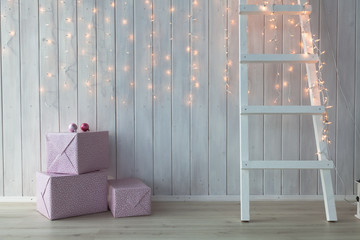 Christmas lights burning on a white wooden background with pink giftboxes and stairs