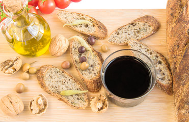Tray with baguette, nuts, olives, oil, glass of vine, tomatoes.