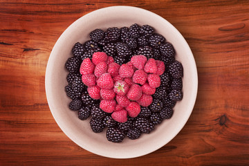 Ceramic plate with heart shaped berries on the middle of the wooden table with clipping path. Top view.