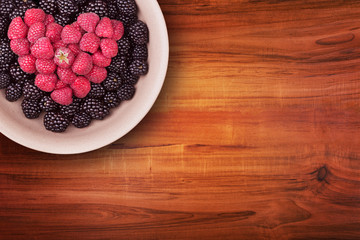 Ceramic plate with heart shaped berries on the left top corner of the wooden table with clipping path. Top view.