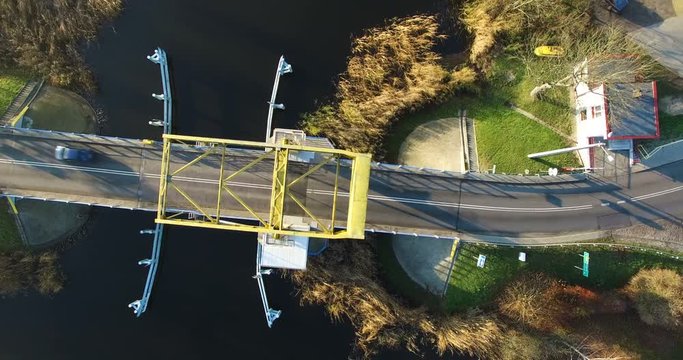 Aerial 4K Yellow single leafed bascule bridge over calm canal water with two cars passing