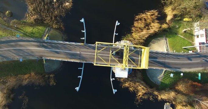 Aerial 4K Yellow single leafed bascule bridge over calm canal water with two cars passing