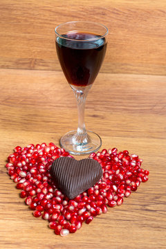 Glass of red wine and heart from pomegranate seeds and chocolate. Declaration of love on Valentine's Day.