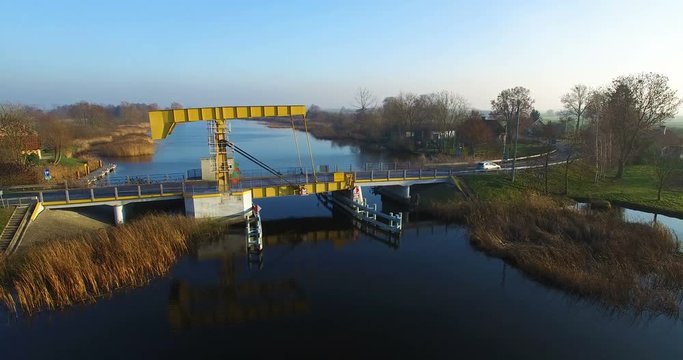 Aerial 4K Yellow single leafed bascule bridge over calm canal water with metallic silver car passing