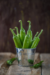 Acute green peppers in an aluminum bucket on old boards