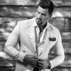 Black-white portrait of young handsome fashionable man in white suit against wooden wall..