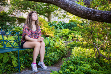 Young sad woman sitting on bench in garden looking up praying