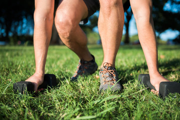 Closeup of young fit man holding dumbbells on grass