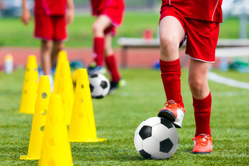 Naklejka premium Kids Football Soccer Training.Young Athlete with Football Ball on Pitch. Child in Red Soccer Uniform Kicking Ball. Boy Practice Dribbling Drills on Sport Grass Field