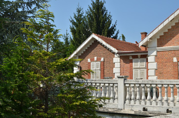 Residential home building of red brick with white wooden blinds surrounded with garden trees