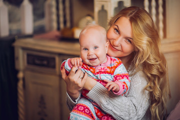 You are my treasure! Side view of cheerful beautiful young woman holding baby girl in her hands and looking at her with love while sitting on the couch at home