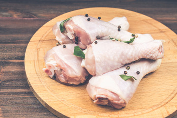 Raw chicken legs with bell pepper on a circular wooden board on