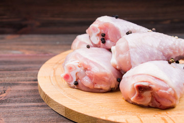 Raw chicken legs with bell pepper on a circular wooden board on