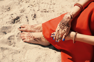 Female legs and hands with henna tattoo on beach sand background