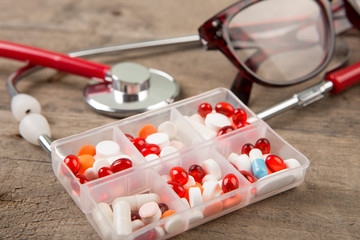 Stethoscope and pills in container on the wooden desk
