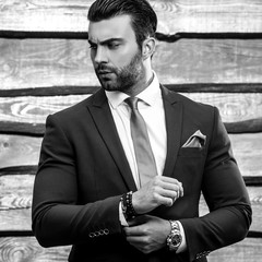 Obraz premium Black-white portrait of beautiful fashionable man in stylish suit against wooden background.