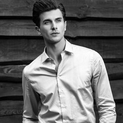 Black-white portrait of young handsome fashionable man against wooden wall.