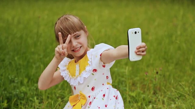 Little girl in a white dress makes selfi on the meadow.