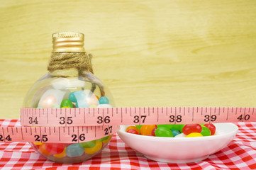 Diet and healthy teeth concept - Colorful candies in bottles and tape measure with shallow depth of field (dof)