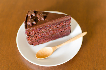 Piece of chocolate cake with wooden spoon on white dish ready to eating