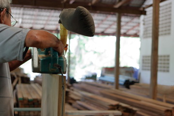 Worker holding a belt sander on vertical of wooden board in carpentry workshop