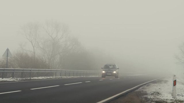 Fog on the road, poor driving conditions. Cars ride on the road and shining lights in the fog. Winter.