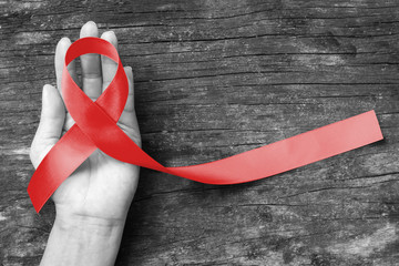 Red ribbon awareness on human hand with aged wood background with clipping path: World aids day: Symbolic concept for raising awareness campaign on people with HIV concept - obrazy, fototapety, plakaty