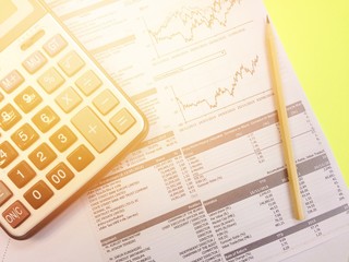 Business, finance or work day background concept : Top view of calculator, pencil and company summary data charts on yellow background