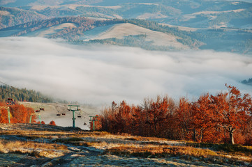 Cableway and ski lifts at autumn mountains background fog and su