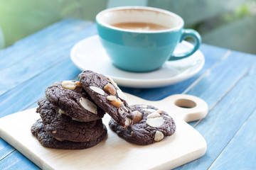 A cup of coffee with chocolate cookie on blue wooden table and green garden background.