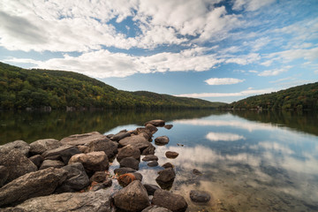 a mountain pond with sky reflection and rocks in the foreground in autumn in New England