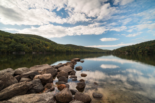 a mountain pond with sky reflection and rocks in the foreground in autumn in New England