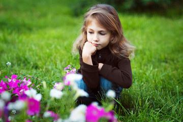 Girl in warm brown jacket sitting on the grass, thinking, and looking at flowers, horizontal.