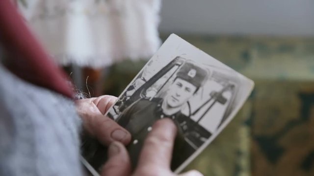 Grandmother holds an old photograph in his hands. Close-up