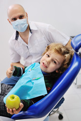 boy with curly red hair sitting in a dental chair and blue holding a green apple in hand. patient at the dentist's background