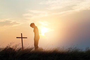 Woman respecting at the cross on the field of sunset background