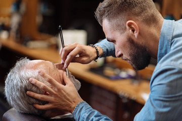 Attractive hairdresser is shaving male beard with the knife