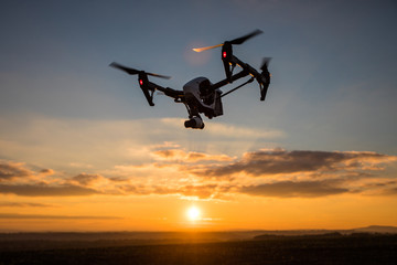 White drone with digital camera flying in sky over field on sunset