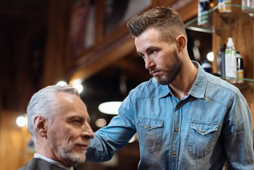 Side view of handsome barber styling clients hair