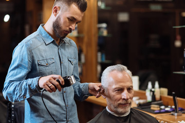 Handsome barber trimming hair of old man