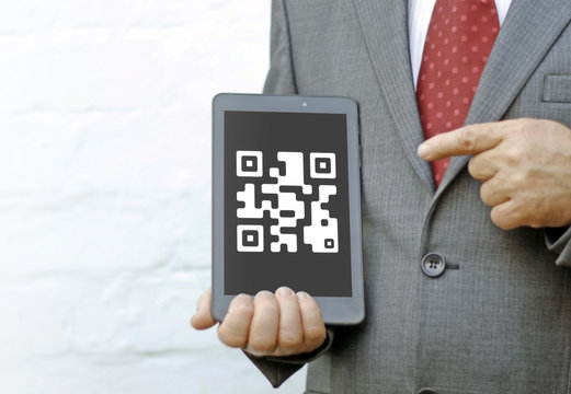 Qrcode icon on the tablet screen. Businessman points finger at qr code icon on the tablet PC. Identification of goods and services by scanning qrcode.