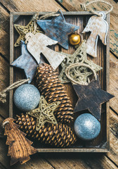 Christmas tree glittering toy stars, balls, pine cones and angel shaped wooden toys in wooden box over rustic background, top view, vertical composition