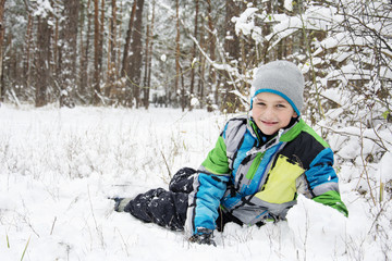 Fototapeta na wymiar In winter, snow-covered pine forest boy lies near the snowdrift.