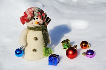 funny snowman in a hat with Christmas toys on a background of snow drifts