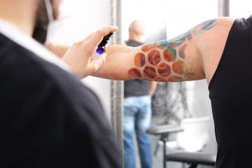 Pielęgnacja tatuażu. Tatuażysta dezynfekuje klientowi nowy rysunek na skórze.