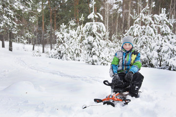 Fototapeta na wymiar In winter, the snow-covered forest boy sitting on a sledge.