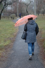 Woman walking down the street rainy autumn - view from the back.