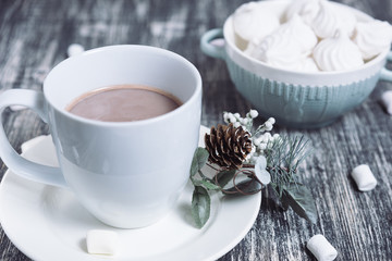 Obraz na płótnie Canvas Hot chocolate with marshmallows. Drink in a white ceramic cup with zephyr on wooden table. Decorative pine branch with the cone on plate, saucer