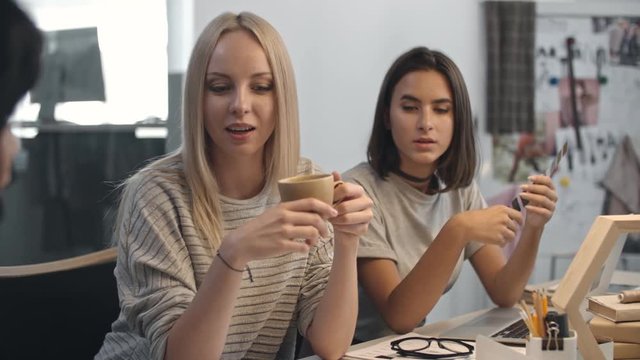 Young attractive women drinking tea and discussing new project in the designers’ office