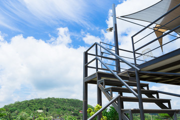 Staircase seen from below against a blue sky with clouds.